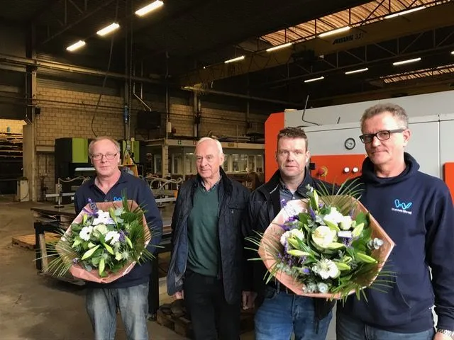 Vier collega’s met bloemen in de werkplaats tijdens het veertigjarig jubileum