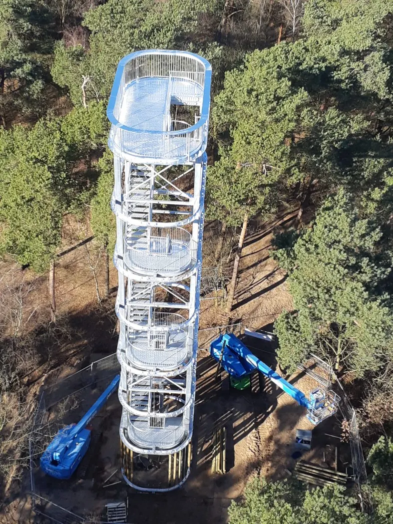 Stalen uitkijktoren in aanbouw tussen de dennen, van bovenaf